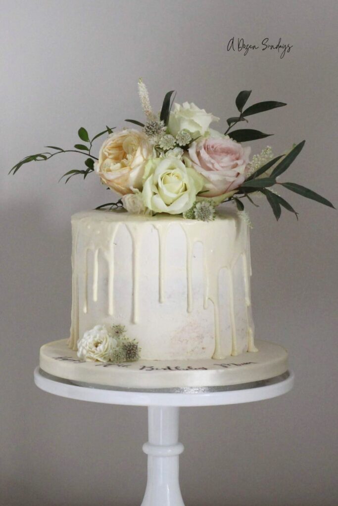 A white chocolate drip cake topped with fresh flowers, ideal for a Mother's Day cake or birthday cake
